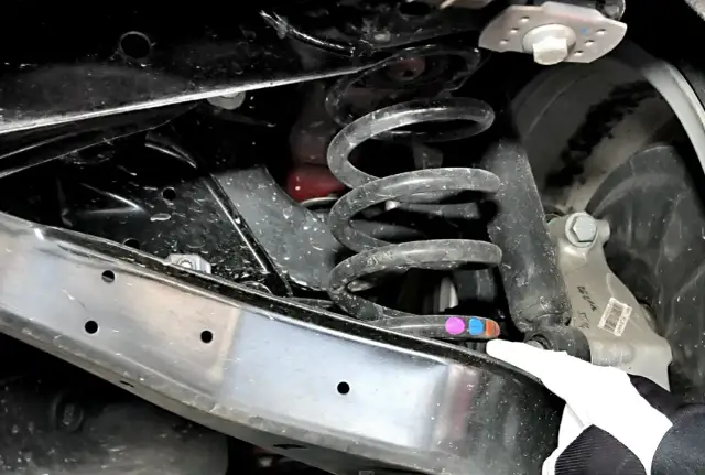 Widoczna pęknięta sprężyna w zawieszeniu auta. Objawy mogą obejmować stukanie, nierównomierne zużycie opon i obniżenie nadwozia.