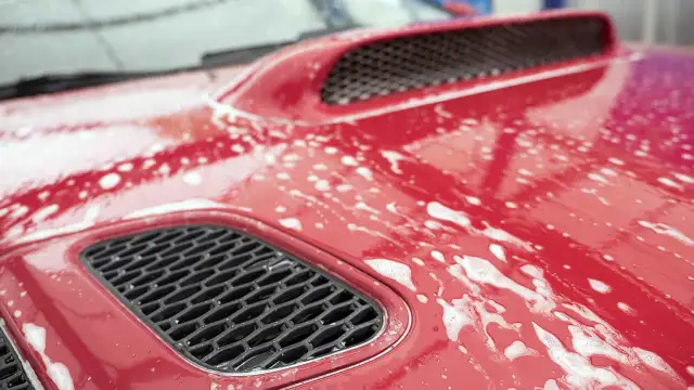 Czerwona maska samochodu pokryta pianą, przygotowana do glinkowania lakieru.