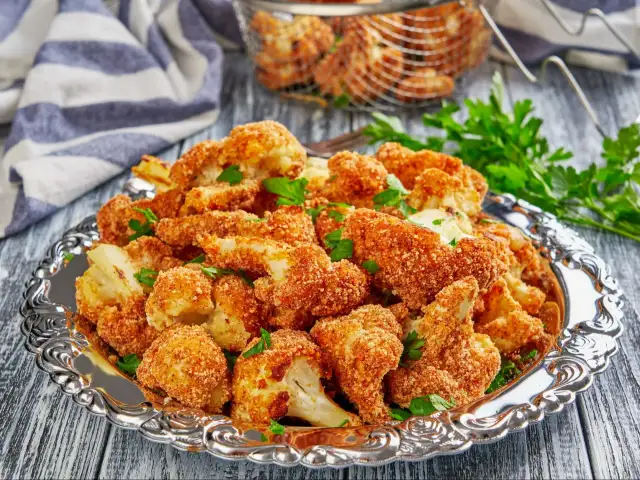 Chrupiący kalafior w panko, podany na ozdobnej tacy, posypany świeżą natką pietruszki. Idealna przekąska!