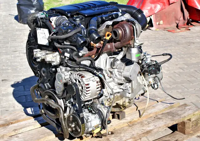 Gotowy do wymiany silnik w samochodzie, z turbosprężarką Garrett i alternatorem, leży na drewnianej palecie.
