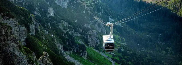 Kolejka linowa w Tatrach na tle skalistych zboczy i lasu.