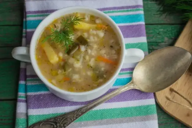 Miseczka zupy z kaszą, ziemniakami i koperkiem, obok łyżka.