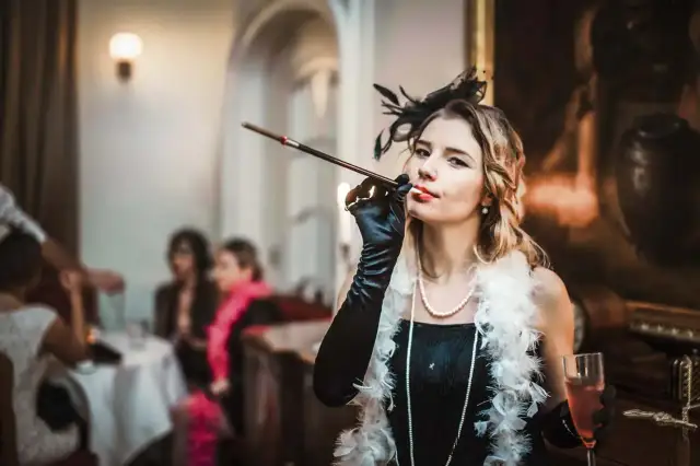 Kobieta w stylu lat 20. z cygaretką i piórami, na tle imprezy.