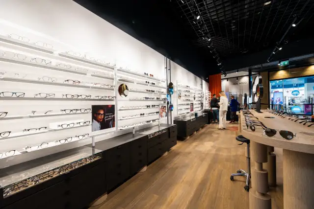 Wnętrze salonu optycznego z wystawami okularów i klientami.