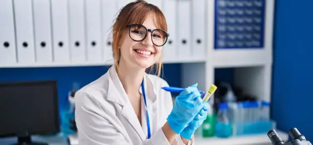 Uśmiechnięta kierowniczka laboratorium w okularach i białym fartuchu, trzymająca probówkę. Zastanawia się, ile zarabia kierownik laboratorium.