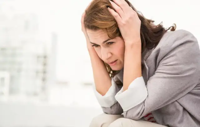 Kobieta z rękami na głowie, wyrażająca niepokój i ból.