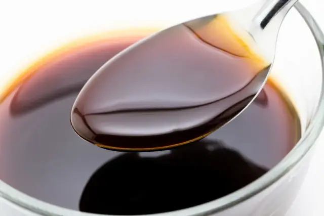 Łyżka z ciemnym, błyszczącym sosem sojowym nad miseczką. Czy sos sojowy jest zdrowy? Zależy od ilości i składu.