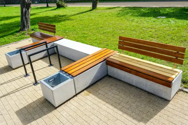 Nowoczesna ławka parkowa z drewnianymi siedziskami i betonową podstawą.
