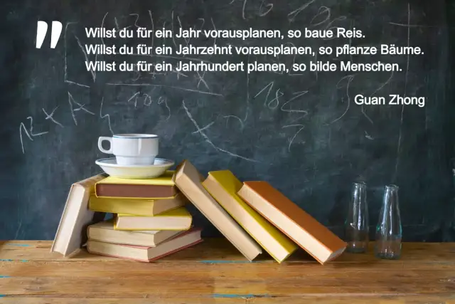 Bücherstapel mit Tasse und zwei leeren Flaschen vor einer Tafel mit Kreideschrift.