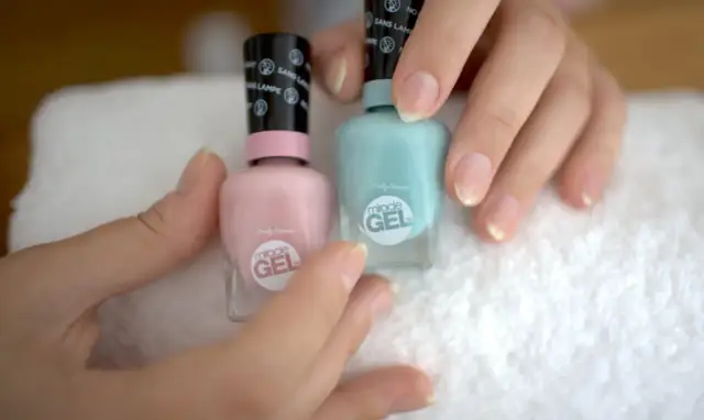 Dłonie trzymają dwa lakiery Sally Hansen Miracle Gel w pastelowych kolorach, gotowe do domowej kuracji paznokci.