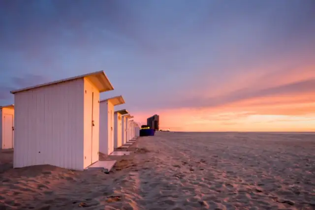 Strandkabinen am Meer bei Sonnenuntergang mit dramatischem Himmel.