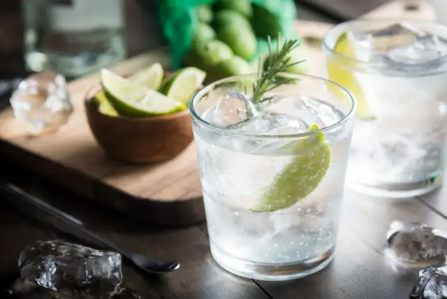 Kto pije gin z tonikiem? Orzeźwiający drink z lodem, limonką i rozmarynem, gotowy do degustacji.