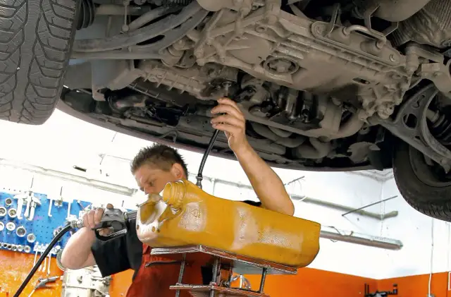 Mechanik wymienia olej w skrzyni biegów DSG, używając żółtego zbiornika i pompy.