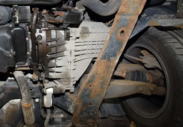 Widok od spodu auta: skorodowane elementy zawieszenia, skrzynia biegów i widoczne przeguby.
