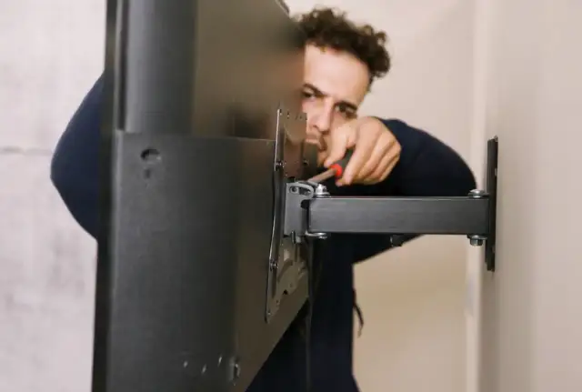 Mężczyzna dokręca śruby podczas montażu TV na ścianie. Widać uchwyt i fragment telewizora.