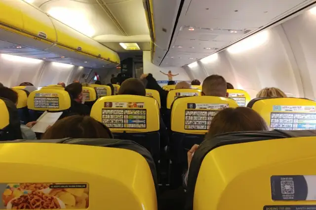 Widok z wnętrza samolotu Ryanair z żółtymi siedzeniami i pasażerami.