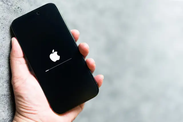 Dłoń trzyma iPhone'a z logo Apple i paskiem postępu. To może być wskazówka, jak wyczyścić pamięć w iPhone, gdy system się ładuje.