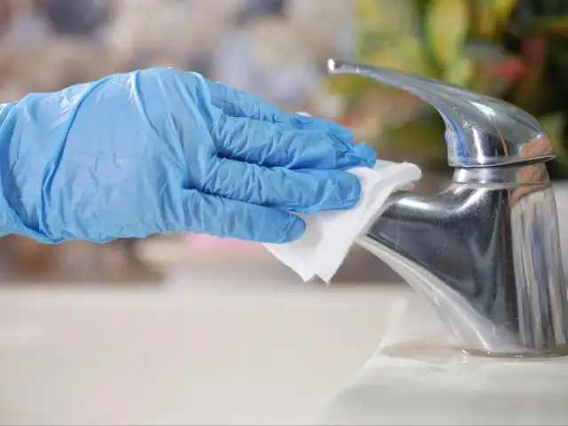 Ręka w niebieskiej rękawiczce czyści białą ściereczką chromowany kran.