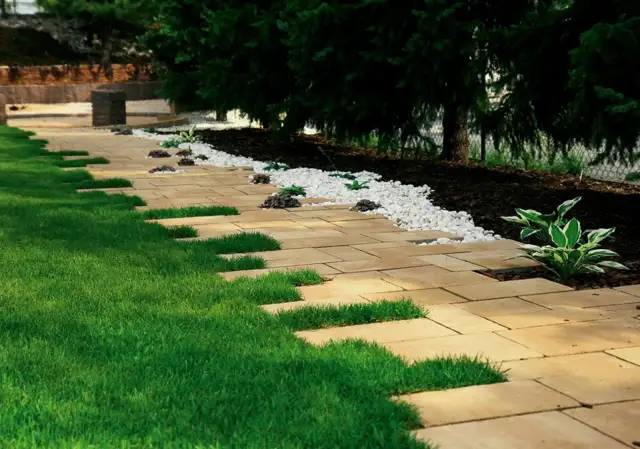 Nowy chodnik w ogrodzie z płyt i trawy, otoczony białym żwirem i zielenią.