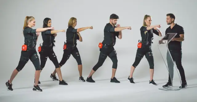 Grupa osób w strojach EMS ćwiczy pod okiem trenera. Dowiedz się, ile kosztuje trening EMS i zacznij swoją metamorfozę!