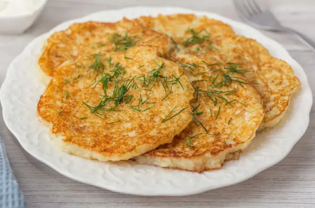 Placki ziemniaczane posypane koperkiem na białym talerzu.