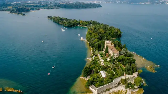 Malowniczy widok na Isola del Garda z pałacem i ogrodami, otoczony turkusową wodą jeziora.