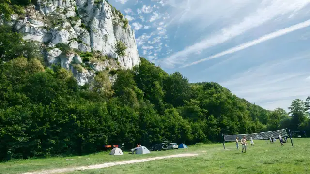 Malownicza brandysówka w Dolinie Będkowskiej. Kemping pod skalną ścianą, ludzie grają w siatkówkę.