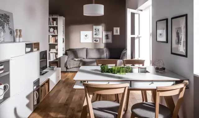 Mała jadalnia inspiracje: nowoczesny salon z szarą kanapą, białymi meblami i drewnianym stołem.