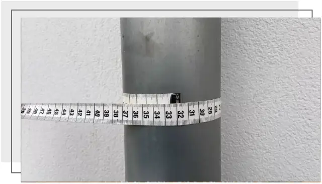 Miarka krawiecka owinięta wokół szarej rury pokazuje, jak zmierzyć średnicę rury. Odczyt wynosi około 32 cm.