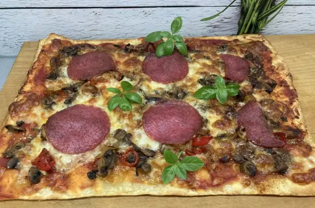 Prostokątna pizza z salami, pieczarkami i papryką, ozdobiona listkami bazylii. Idealne dodatki dla miłośników klasyki.
