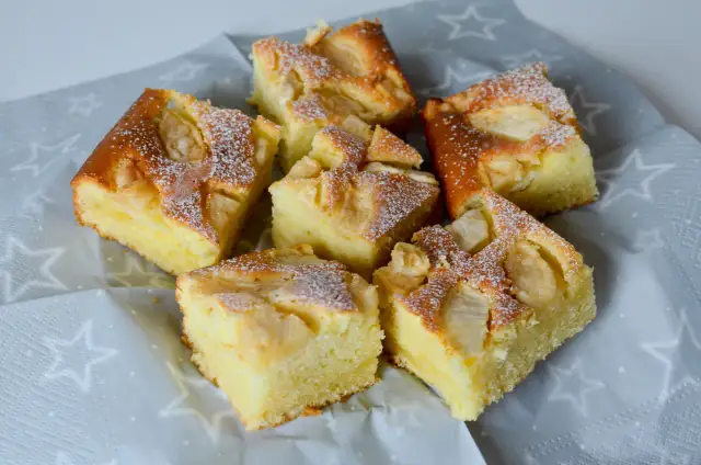 Pyszne ciasto z jabłkami i skyrem, posypane cukrem pudrem, prezentuje się apetycznie na szarej serwetce w gwiazdki.