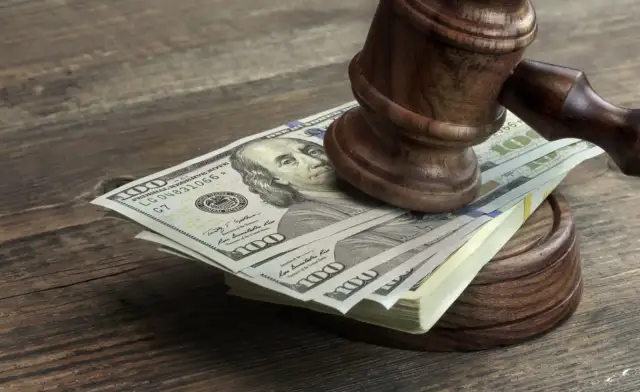 Młotek sędziowski na stosie banknotów 100-dolarowych. Pytanie: ile procent bierze prawnik od wygranej sprawy?