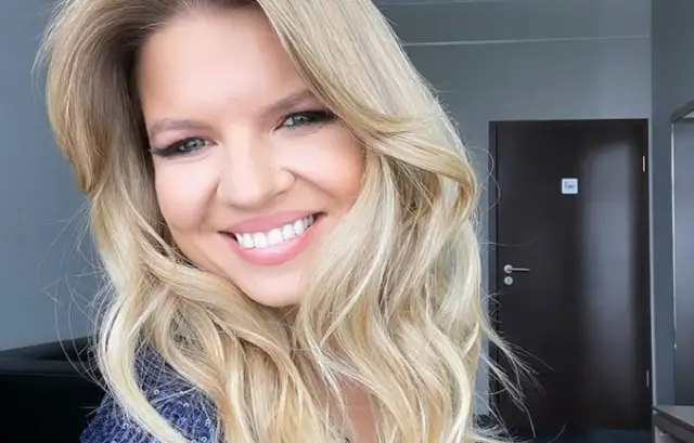 Uśmiechnięta blondynka, prowadząca "Rolnik szuka żony", z falowanymi włosami i w błyszczącej bluzce.