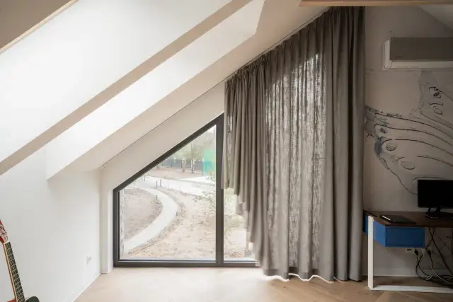 Eleganckie karnisze na skośne okna idealnie komponują się z szarymi zasłonami, tworząc przytulną atmosferę w pokoju na poddaszu.