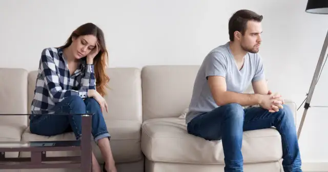 Para, siedząca na kanapie, zamyślona, zastanawia się, jak przeprosić faceta sms. On siedzi obok, odwrócony.