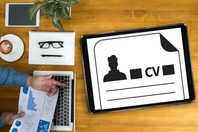 Tablet z ikoną CV i sylwetką mężczyzny, obok laptop, notatnik, okulary i kawa.