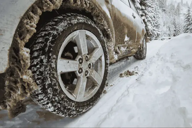 Samochód z napędem 4WD vs AWD na zaśnieżonej drodze. Błoto i śnieg oblepiają koło, sugerując trudne warunki terenowe.