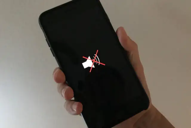 Dłoń trzyma czarny telefon z wyciszonym głośnikiem. Gdy dźwięk nie działa, warto dowiedzieć się, jak wyczyścić głośnik w telefonie.