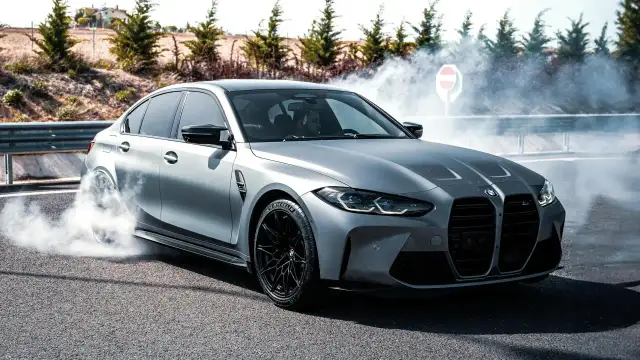 Srebrne BMW M3 G80 w poślizgu, z opon dymiących na asfalcie.