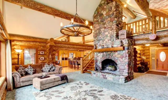 Przytulny salon w stylu country glam z kamiennym kominkiem, drewnianymi belkami i wygodną kanapą.