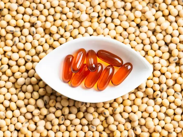 Kapsułki z lecytyną sojową na tle ziaren soi. Czy lecytyna sojowa jest szkodliwa?