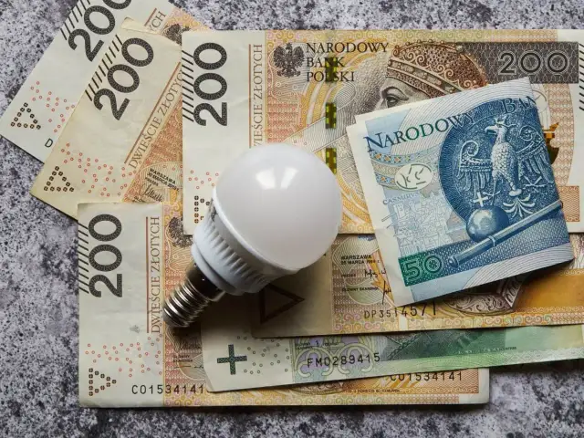 Żarówka LED na stosie polskich banknotów 200 zł i 50 zł. Symbolizuje koszty energii, prąd na kartę cennik.