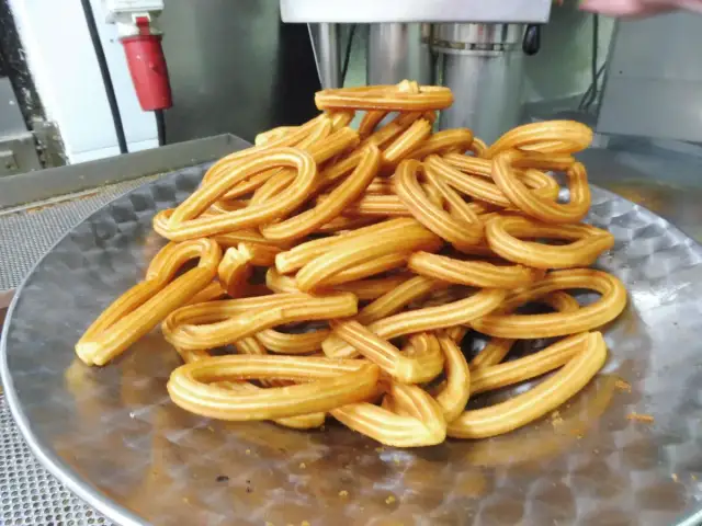 Montón de churros dorados en forma de lazo sobre un plato metálico.
