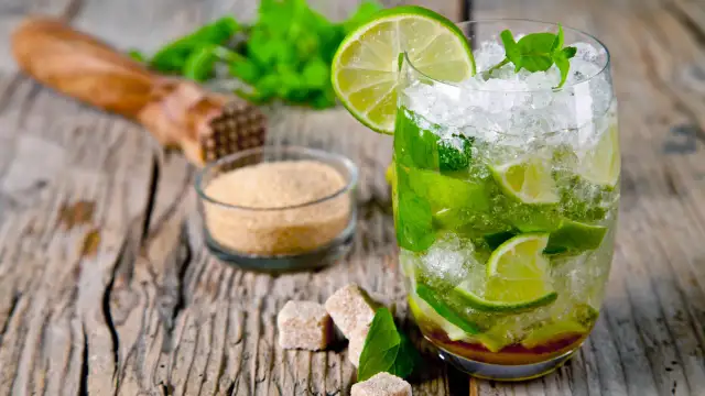 Orzeźwiający Mojito przepis: szklanka z lodem, limonką i miętą, obok cukier trzcinowy i muddler. Idealny na lato!
