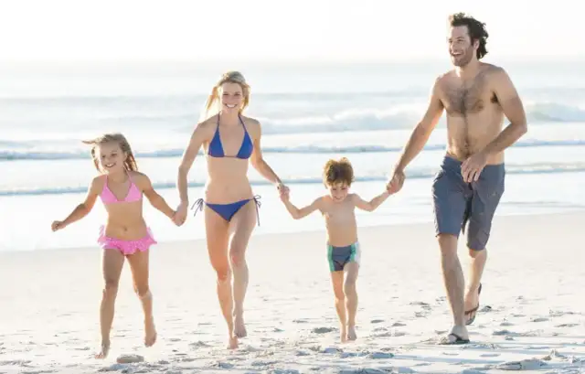 Szczęśliwa rodzina biegnie plażą, szukając pomysłów, gdzie nad morze z dziećmi tanio. Słońce, piasek i radość dzieci.