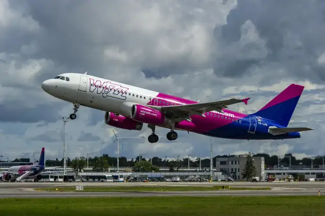 Samolot Wizz Air z różowymi silnikami startuje na tle chmur.