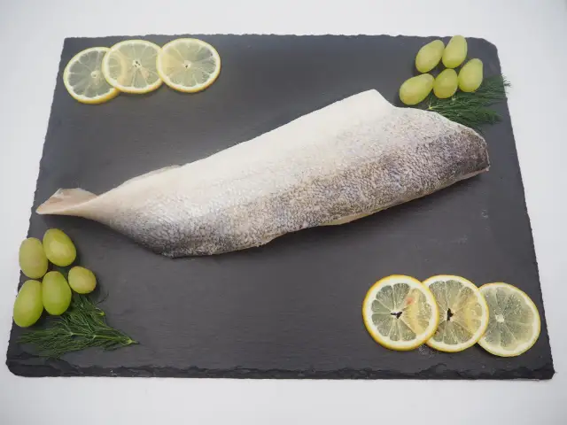 Filet ryby na czarnej desce z plasterkami cytryny, winogronami i koperkiem.