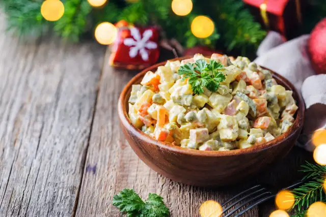 Sałatka jarzynowa w drewnianej misce, udekorowana natką pietruszki, na tle świątecznych lampek.