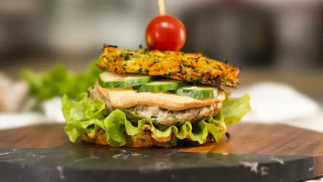 Burger z warzywną bułką, kotletem, ogórkiem, sosem i pomidorkiem na wykałaczce.