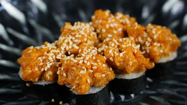 Pyszne sushi z tatarem z łososia, posypane sezamem, prezentuje się apetycznie na ciemnym talerzu.